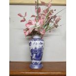 A blue and white willow pattern vase with silk flowers.