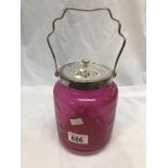 A cranberry glass jar with metal lid and handle.