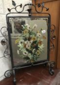 A wrought iron firescreen with hand painted mirror insert.