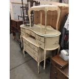 A cream dressing table (no mirror) with a matching chest of drawers and dressing table stool.