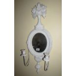 An oval mirror in painted frame with attached candle sconces.