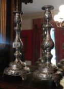 A pair of tall ornate silver candlesticks.