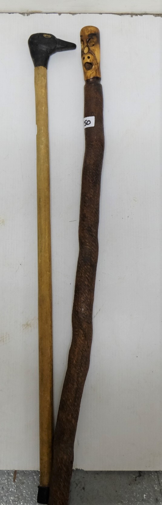 2 wooden walking sticks – 1 mounted with a carved ducks head & 1 with figure of a “spook”, on a