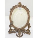 Mid 20th C decorative brass table mirror, oval shaped and bevelled with floral mounts, the base