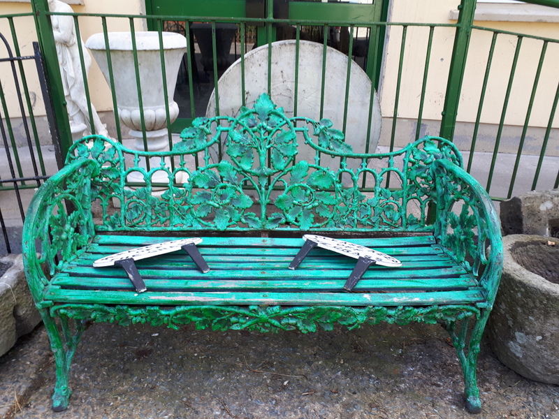 Cast iron three seater metal garden seat with wooden slats decorated with oak leaves.