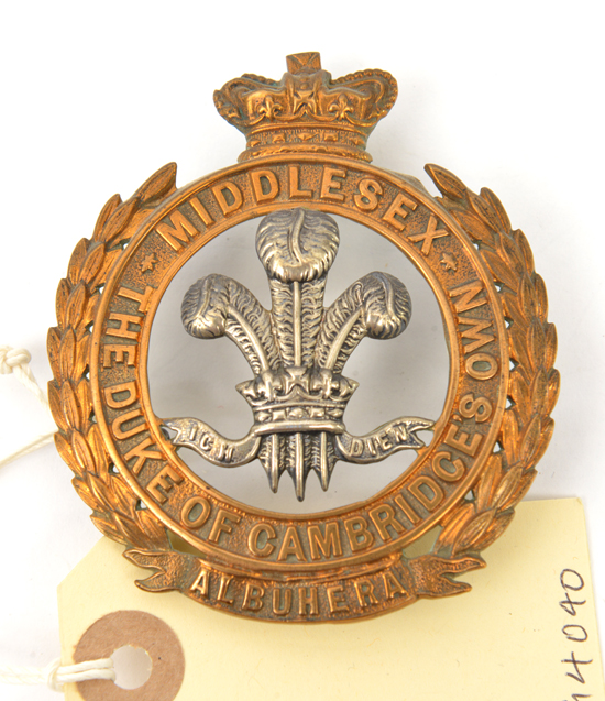 A Vic bi-metal puggaree badge of The Middlesex Regt, POW’s feathers in crowned title and wreath with