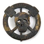 A German WWI style oxidised bronze badge, depicting a skull over crossed stick grenades, the whole