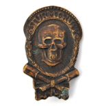 A German WWI style oxidised bronze badge, depicting a skull within a wreath above crossed stick