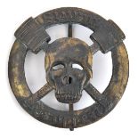 A German WWI style oxidised bronze badge, depicting a skull over crossed stick grenades, the whole