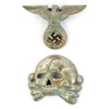 A Third Reich “old style” peaked cap nickel eagle and skull insignia, the skull marked “RZM” and “ST