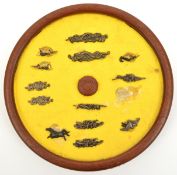 A collection of 13 Japanese menuki, mounted for display on a round wooden frame, GC (2 loose).