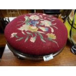 A Victorian circular walnut upholstered wool work topped stool raised on carved feet.