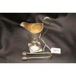 A George III silver helmet shaped footed cream jug on raised base, engraved garland style