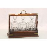Mahogany cased three bottle Tantalus with brass detailing and cut glass bottles