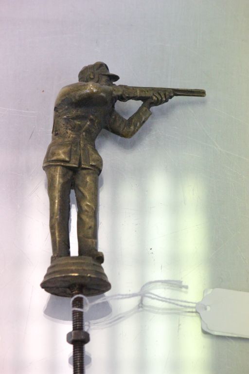 A brass car mascot of a shotgun shooter clay pigeon