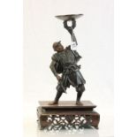 Bronze model of a Japanese Samurai warrior holding a dish aloft, on a carved Hardwood base