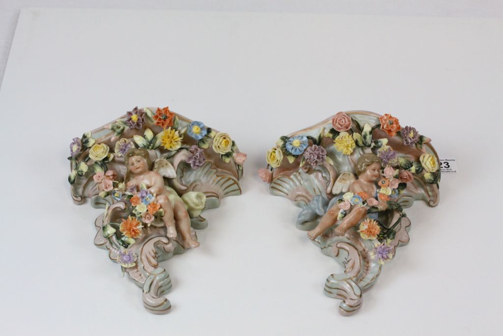 A pair of Continental hand painted cherub wall pockets, the cherub laying amongst roses, dahlias and