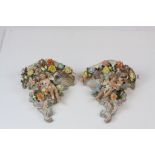A pair of Continental hand painted cherub wall pockets, the cherub laying amongst roses, dahlias and