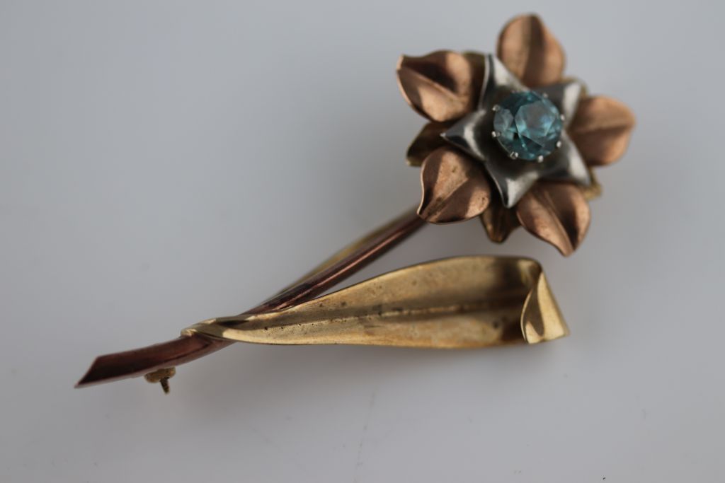 A blue topaz 9ct tri colour gold flower brooch, the round mixed cut claw set flower head centre blue