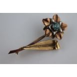 A blue topaz 9ct tri colour gold flower brooch, the round mixed cut claw set flower head centre blue