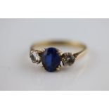A synthetic blue sapphire and white stone three stone 9ct yellow gold ring, claw settings, ring size