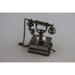 A novelty white metal telephone figurine, modelled as a late 19th century telephone, chain attaching