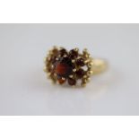 A garnet 9ct yellow gold fancy flower head dress ring, the centre round mixed cut claw set garnet