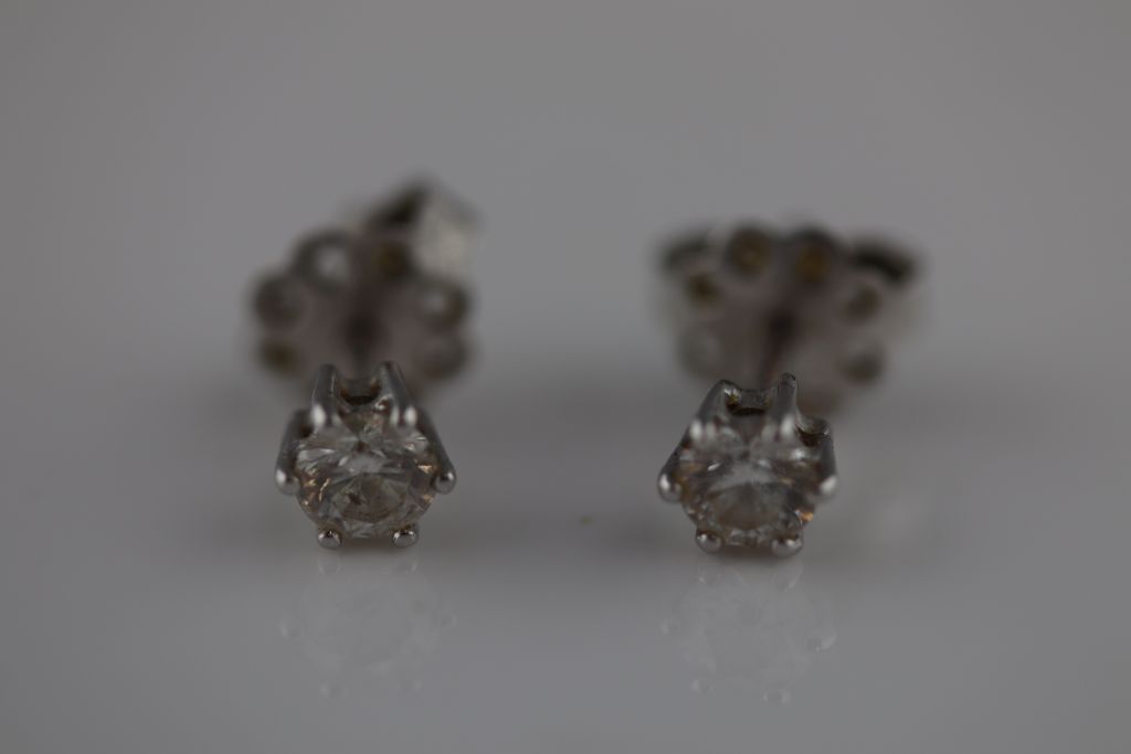 A pair of diamond solitaire white metal stud earrings, each round brilliant cut diamond weighing