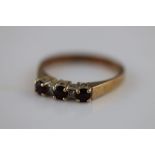 A garnet three stone 9ct yellow gold ring, the three round mixed cut claw set garnets with diamond