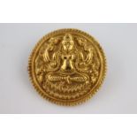 A late 19th century Indian yellow gold circular brooch depicting crossed legged figure cast in