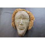 Carved tribal mask with straw hair, approximately 27cm by 22cm