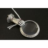 A silver hand held magnifying glass in the form of a hand with ruby collar.