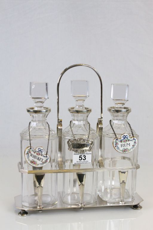 Silver plated three bottle Tantalus with original bottles, two with ceramic labels, the other with a