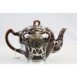 An Art Nouveau treacle glaze teapot with white metal overlay, the central flower motif with