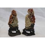 A pair of carved Oriental hardstone figurines depicting elders seated in floral tree, raised on