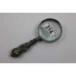 White metal magnifying glass with repousse cherubs kissing and scroll decoration to handle, silver