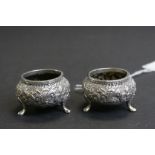 Pair of white metal salts raised on three feet, repousse foliate scroll decoration, height