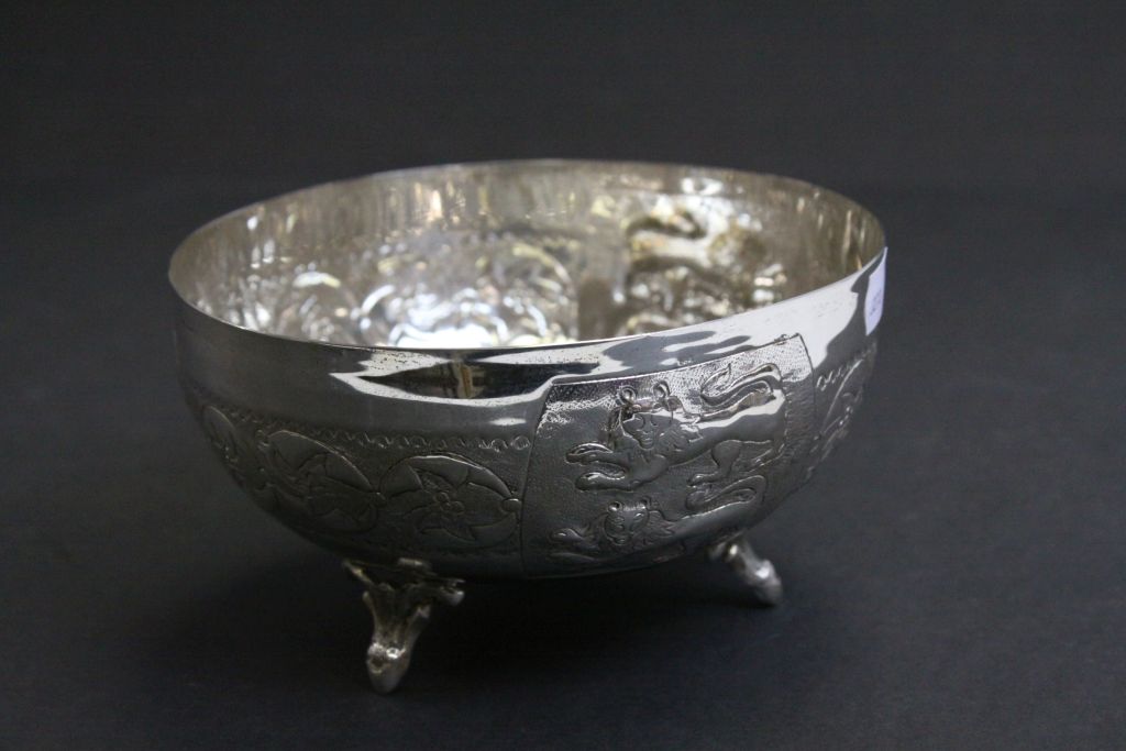 White metal bowl raised on three feet, repousse lion and stylised floral decoration, approximately