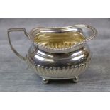 Early George V silver cream jug raised on four ball feet, gadrooning to lower half and rim,