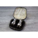 Pair of cased silver pepper pots of baluster form with pierced scroll design border, raised on