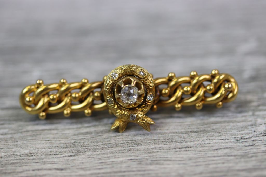 Victorian Etruscan Revival diamond yellow metal bar brooch, the central wreath motif with round