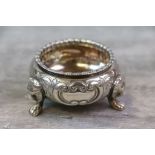 Edwardian silver open salt raised on three lion mask and paw feet, repousse floral decoration to