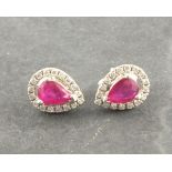 A pair of ruby and diamond ear studs, the pear shaped stone within a band of diamonds, set in 18ct