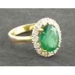 An emerald and diamond dress ring, the oval central stone within a band of diamonds and set in an