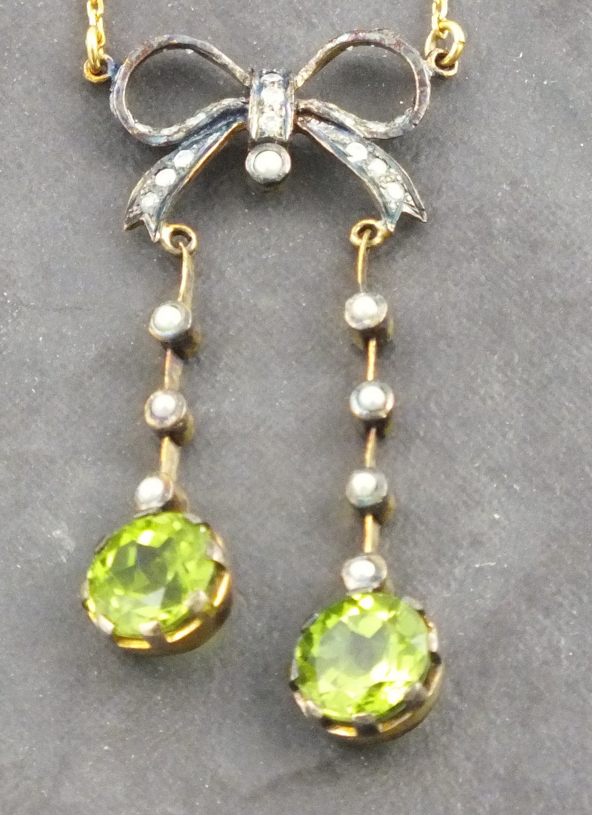 A peridot and seed pearl pendent necklace, the drops suspended from a bow