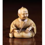 A Meiji Netsuke carved as a seated man holding a fan,