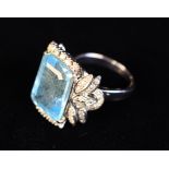 A White Gold Ring with large emerald-cut Aquamarine Coloured Stone flanked by leaves encrusted with