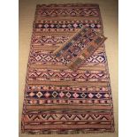 A Kelim Carpet woven in red, pink, browns, buff, ivory and dark blue with geometric bands,