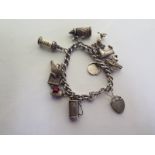 A silver charm bracelet with various charms including golf clubs, poodle, ship in a bottle etc -