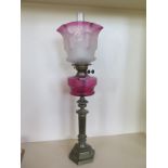 An oil lamp with an etched cranberry tinted shade and cranberry font, 81cm tall